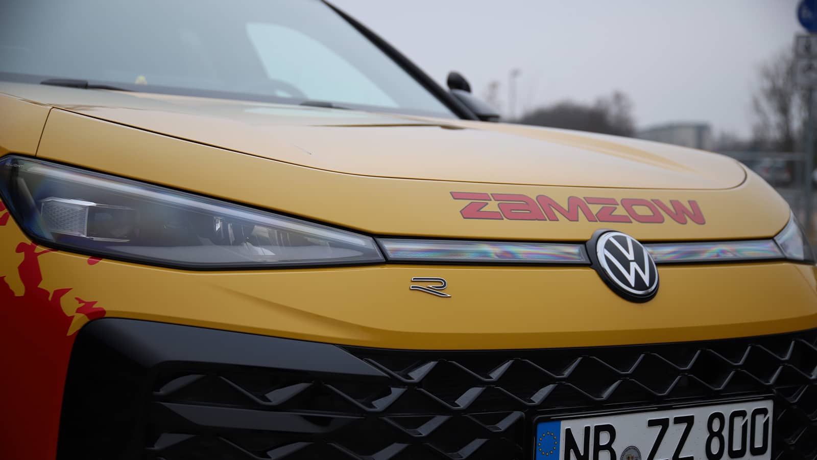 Front-Seitenansicht des VW T-Roc in Neubrandenburg: Gelbes R-Line Modell mit auffälliger Zamzow-Folierung und schwarzem Kühlergrill.